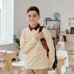 A smiling schoolboy confidently standing in a modern classroom with his backpack.